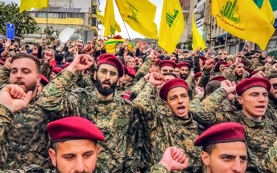 真主黨支持者與武裝成員在街頭集會，高舉旗幟並呼喊口號，呈現群眾動員氛圍