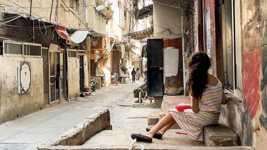 巴勒斯坦難民營狹窄巷道與住宅環境，一名女孩坐在門前，呈現長期居住社區的日常生活景象