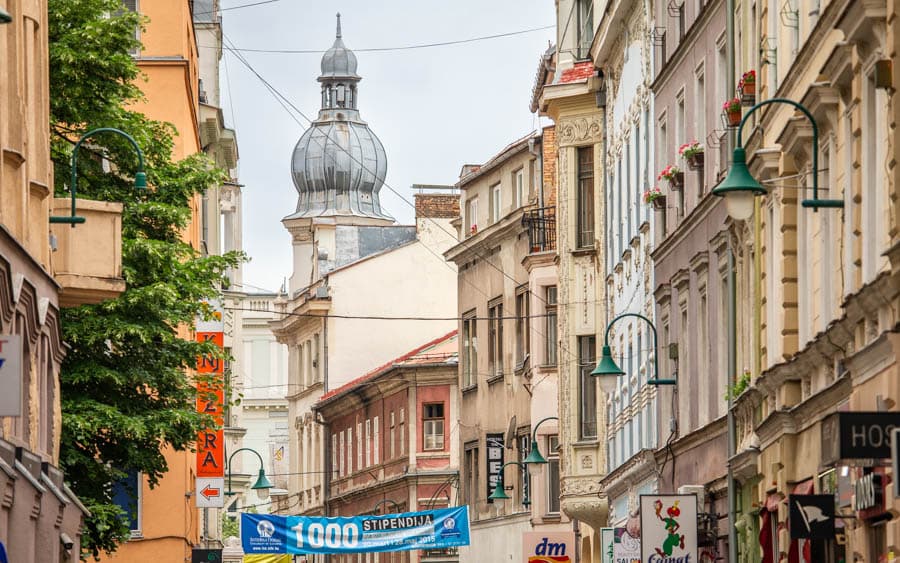 奧匈帝國（西方）邊： 照片中所處的位置正是費爾哈迪亞街。這裡的建築呈現典型的中歐風格，如新古典主義或波西米亞風格，街道較寬闊，兩旁有像是藥妝店 或西式咖啡館等現代商店。