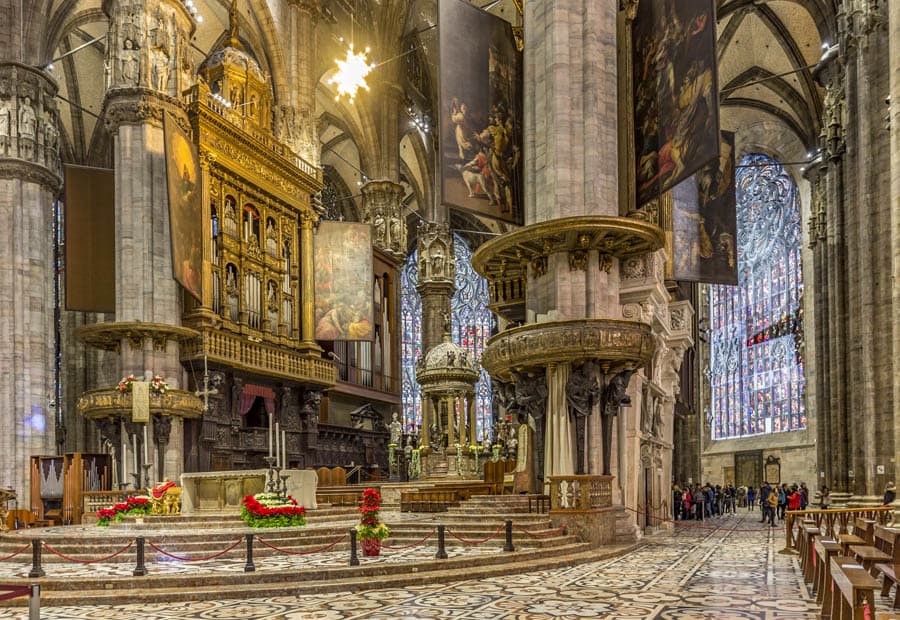 義大利米蘭主教座堂（Duomo di Milano）內部祭壇區，可見巨大的管風琴、大理石柱與懸掛的聖像畫。