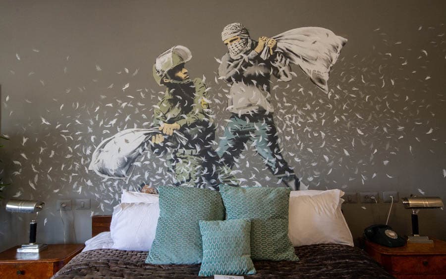 伯利恆圍牆飯店客房內BANKSY的作品:• 枕頭大戰(Pillow Fight):位於「Banksy 房」內,描繪一名巴勒斯坦人與一名以色列人士兵拿著枕頭對戰,象徵著以羽毛代替子彈的和平願望。